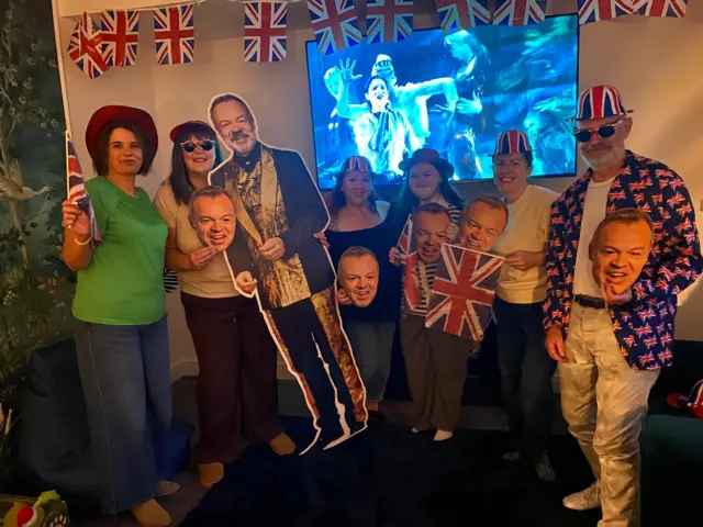 Hen party photo with union flags, Graham Norton masks and Eurovision on TV in the background