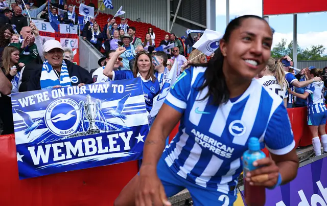 Manuela Vanegas of Brighton & Hove Albion celebrates victory with fans displaying a sign reading 'We're On Our Way To Wembley'