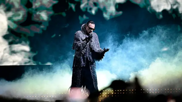 Alis standing on stage in front of smoke and a dark background singing into a mix