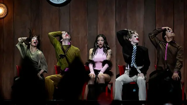 Dara sat in between two people on either side of her who are dancing as she sings
