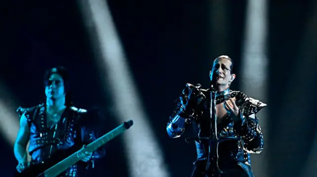 Two men on stage performing wearing black leather studded outfits