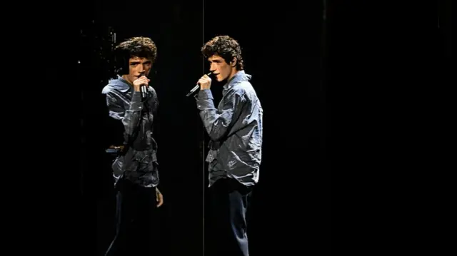 Daniel standing against a black background in front of a mirror