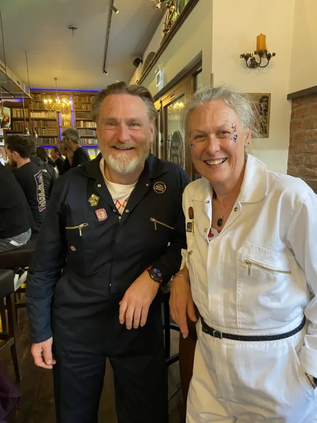 A man and a woman in jumpsuits smiling at camera.