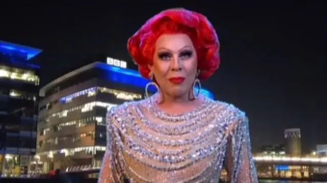 Headshot of La Voix in a sparkly dress in front of a BBC office by a river