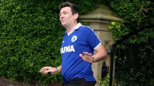 Andy Burnham waves at the media as he goes for a run in an Everton shirt on Friday