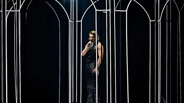 Man in leather vest sings among LED lights resembling pillars