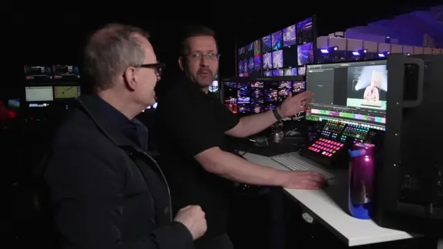 Two men looking at a computer in a dark room full of screens