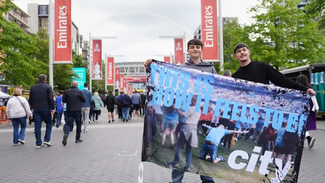 Two City fans hold up a Manchester City banner on Wembley Walk