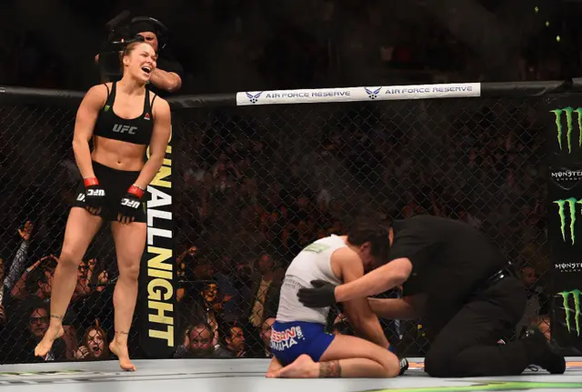 Ronda Rousey jumps in the air as a referee checks on Cat Zingano in the UFC octagon
