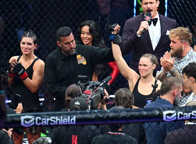 Ronda Rousey (right) having her hand raised next to Gina Carano (left)