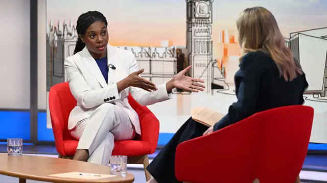 Kemi Badenoch (L) in a white pantsuit sitting on a red chair speaks to presenter Laura Kuenssberg (R) sitting on a matching chair with her back to the camera
