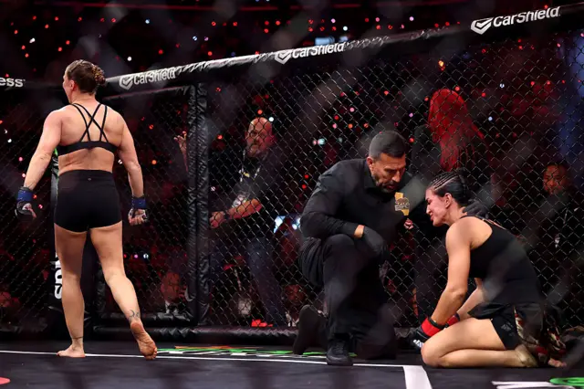 Ronda Rousey celebrates as Gina Carano is checked on by the referee