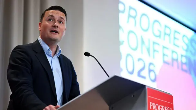 Wes Streeting speaking from behind a lectern, there is a microphone in front of him