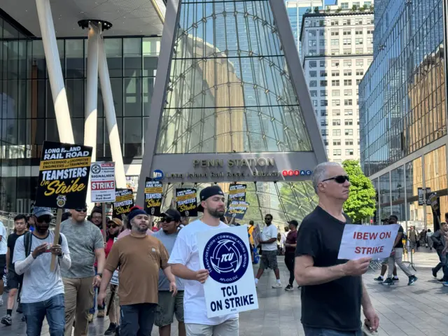 Striking rail workers hold signs outside the entrance to Penn Station in New York