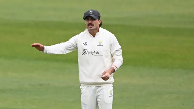 Glamorgan captain Kiran Carlson, in the field and wearing a cap with the Glamorgan badge on it, gestures to a teammate who is not pictured