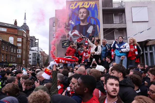 Arsenal fans wave scarves and set off flares outside the ground