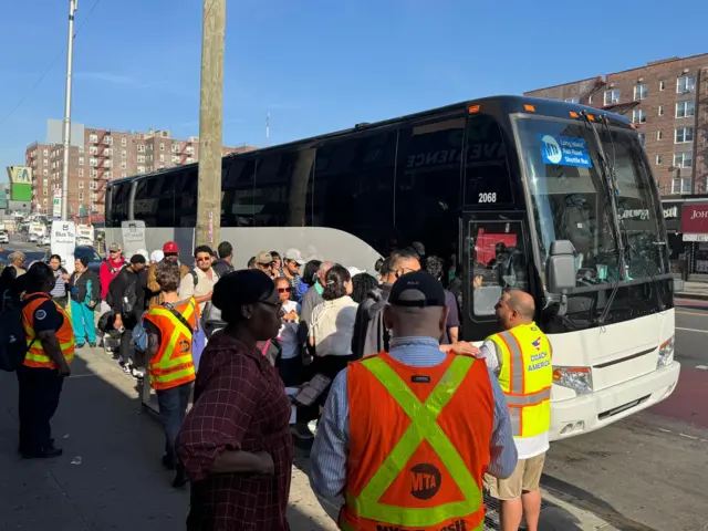 People in yellow and orange vests direct commuters onto shuttle buses
