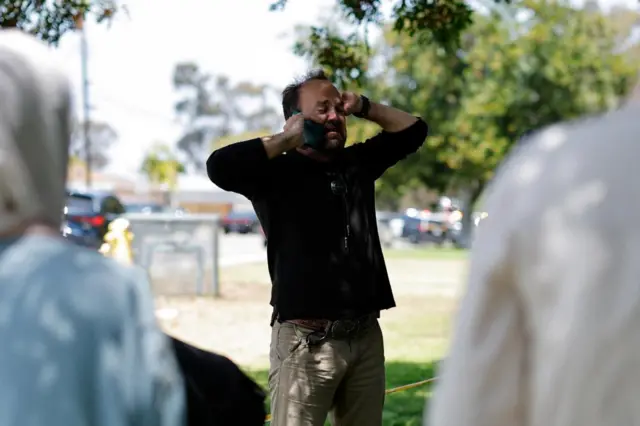 A man on the phone appears upset as he stands outside the crime scene