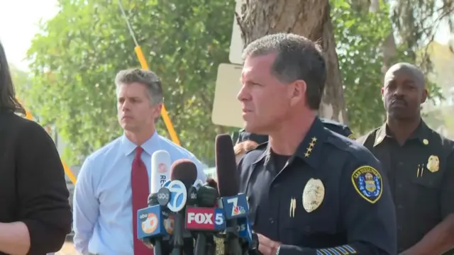 Police chief behing multiple microphones, surrounded by officers