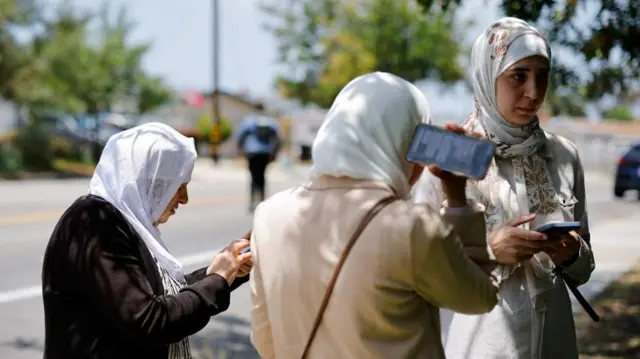 A group of women at the scene use their phones to follow updates