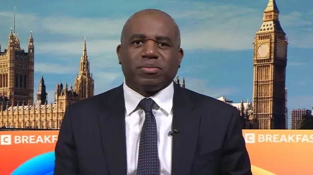 Deputy Prime Minister David lammy wearing a black suit speaking to BBC Breakfast with a backdrop of the Houses of Parliament