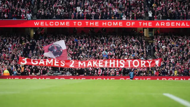 Arsenal fans hold up a banner with the words '3 games 2 make history'