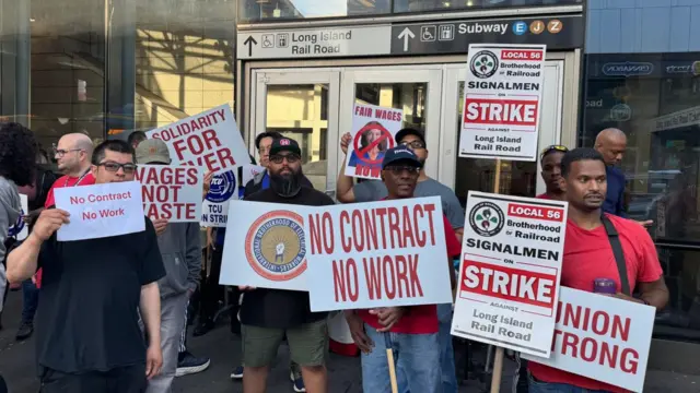Striking rail workers hold signs demanding a new contract