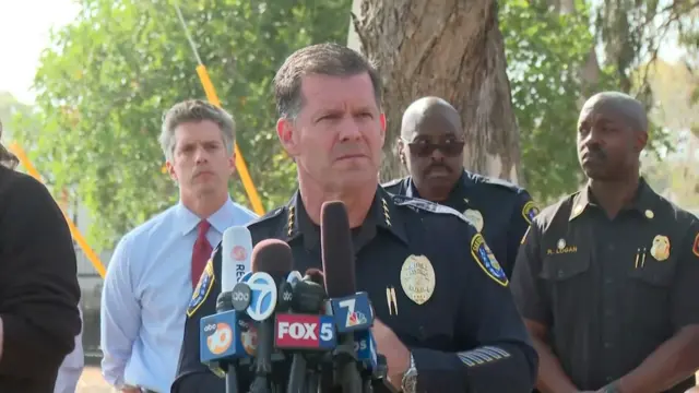 Police chief in uniiform outside behind microphones surrounded by other officers