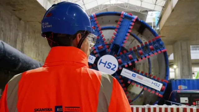 A person in hi-vis clothing stood in front of a large machine with HS2 branding