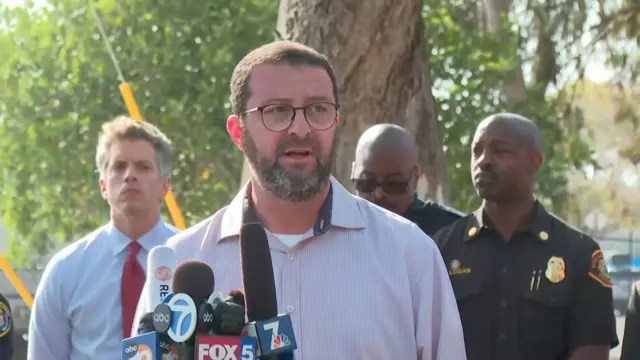 Imam in glasses and button-down light shirt behind microphones