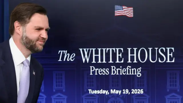 Vance walks past a TV screen announcing today's briefing
