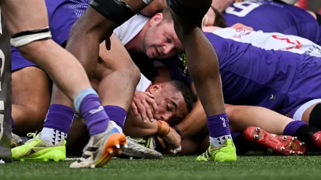 Juarno Augustus (centre) holds the ball over the line under a pile of bodies