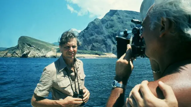 David Attenborough on a boat with cliffs in the background