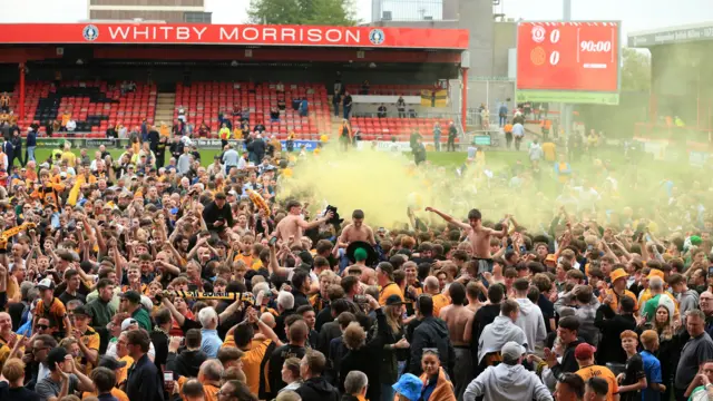 Cambridge United fans celebrating on the pitch at Crewe