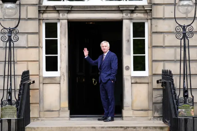 Ivan McKee in blue suit waves on the steps of Bute House