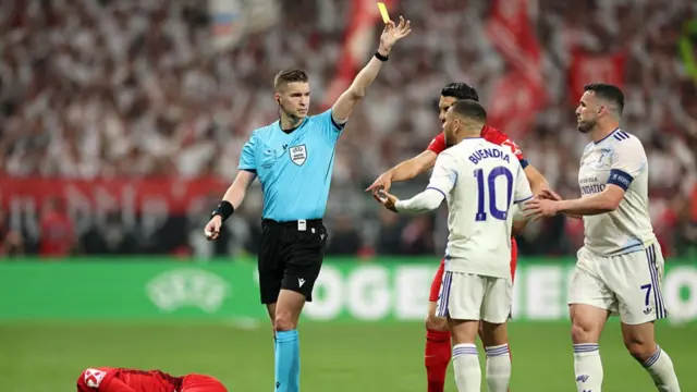 Referee Francois Letexier shows a yellow card to Emi Buendia