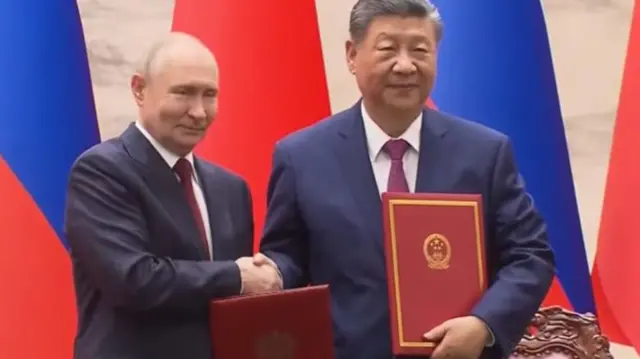 Putin and Xi shake hands while holding red folders