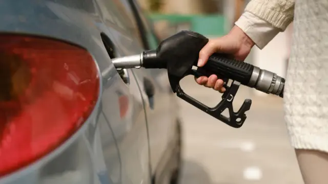 Unrecognizable woman using gas pump to add fuel to her car during energy crisis