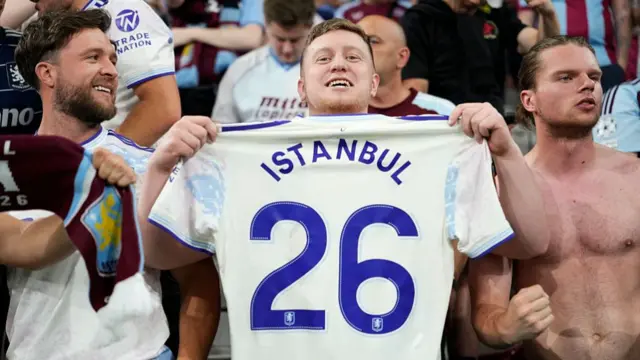 An Aston Villa fan holds a shirt with "Istanbul 26" printed on it