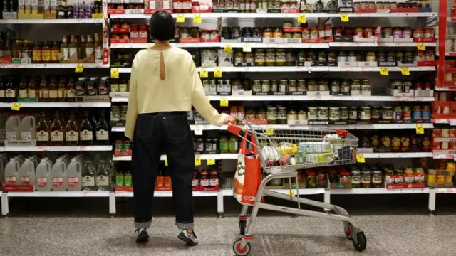 A woman holds a trolley and looks at a supermarket shelf