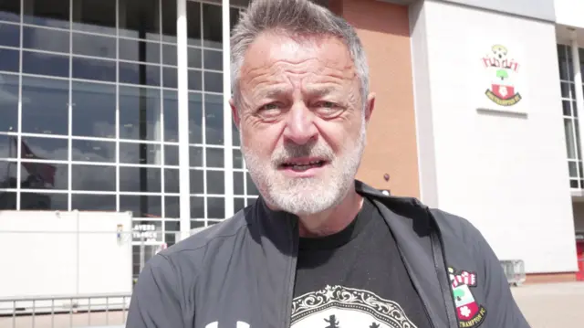 A man wearing a grey Southampton FC jacket stood in front of the St Mary's football stadium