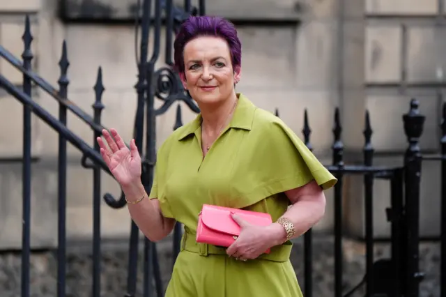 Angela Constance in green suit carrying pink bag, gives a wave.