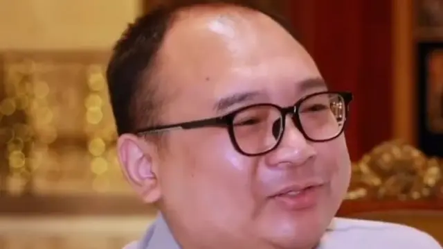 A middle-aged man with a round face and black spectacles
