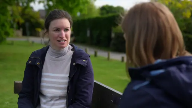 Mary Sutherland, a mother of a young child. She is sitting on a bench in a park speaking to BBC correspondent Colletta Smith. She is wearing a navy coat and a beige and white striped jumper