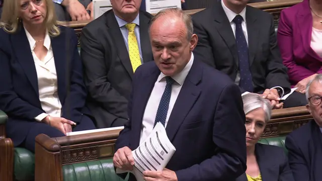 Ed Davey holds several pieces of paper up as he speaks in the House of Commons