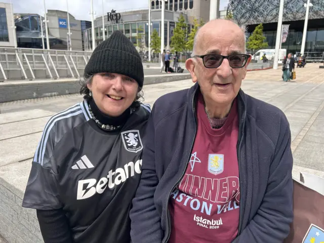 Diane wears a black beanie had and an Aston Villa top, Colin has dark glasses and a claret Aston Villa winners top under a blue fleece