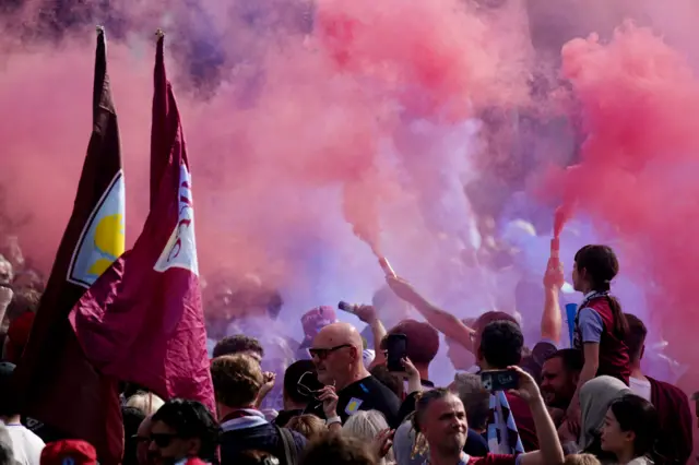 Red smoke emanates from flares and large Villa flags are held aloft as fans gather for the parade.