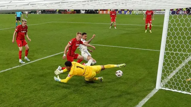 Morgan Rogers on the floor with the Freiburg goalkeeper sprawled nearby as the ball heads towards the net