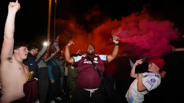Villa fans celebrate - one in the centre raises a flare while others film