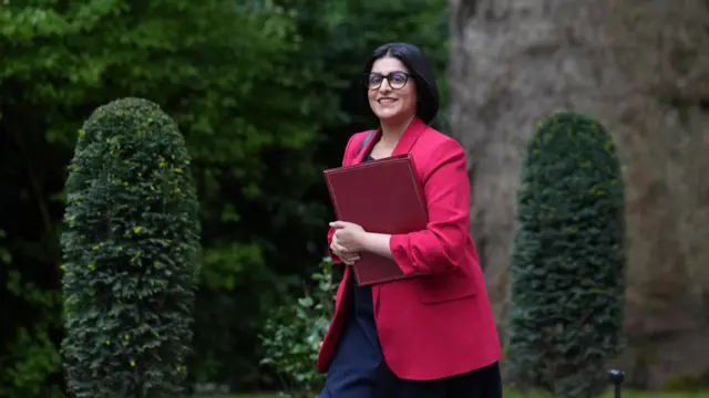 Home Secretary Shabana Mahmood wears a red blazer and carries a red folder as she walks towards Downing Street for a meeting